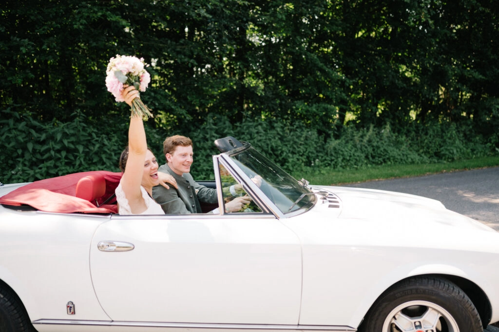Brautpaar fährt im offenen Hochzeitscabrio.