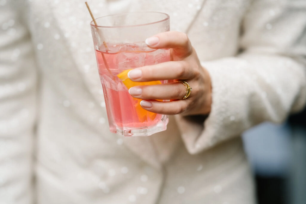 Braut hält ein rosa Getränk im Glas.
