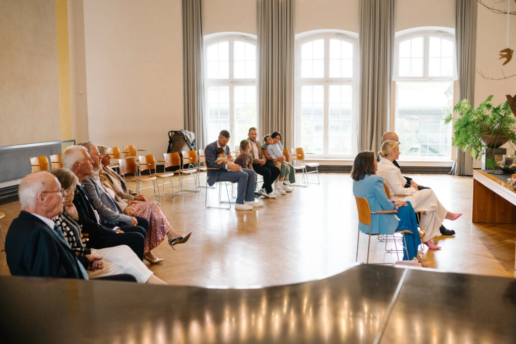 Gäste sitzen während der Trauung im hellen Saal.