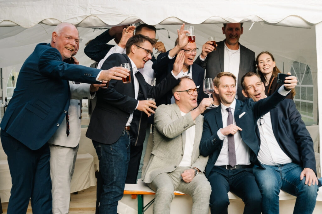 Hochzeitsgäste machen gemeinsam Selfies vor dem Festzelt.