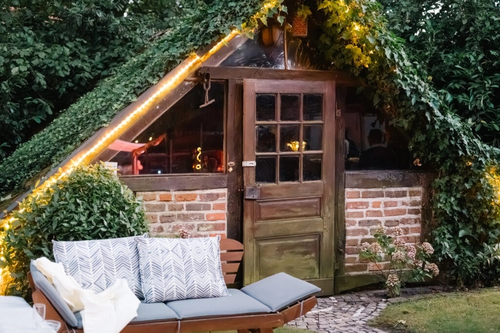 Kleine Gartenhütte mit Lichterkette und Sitzbank.