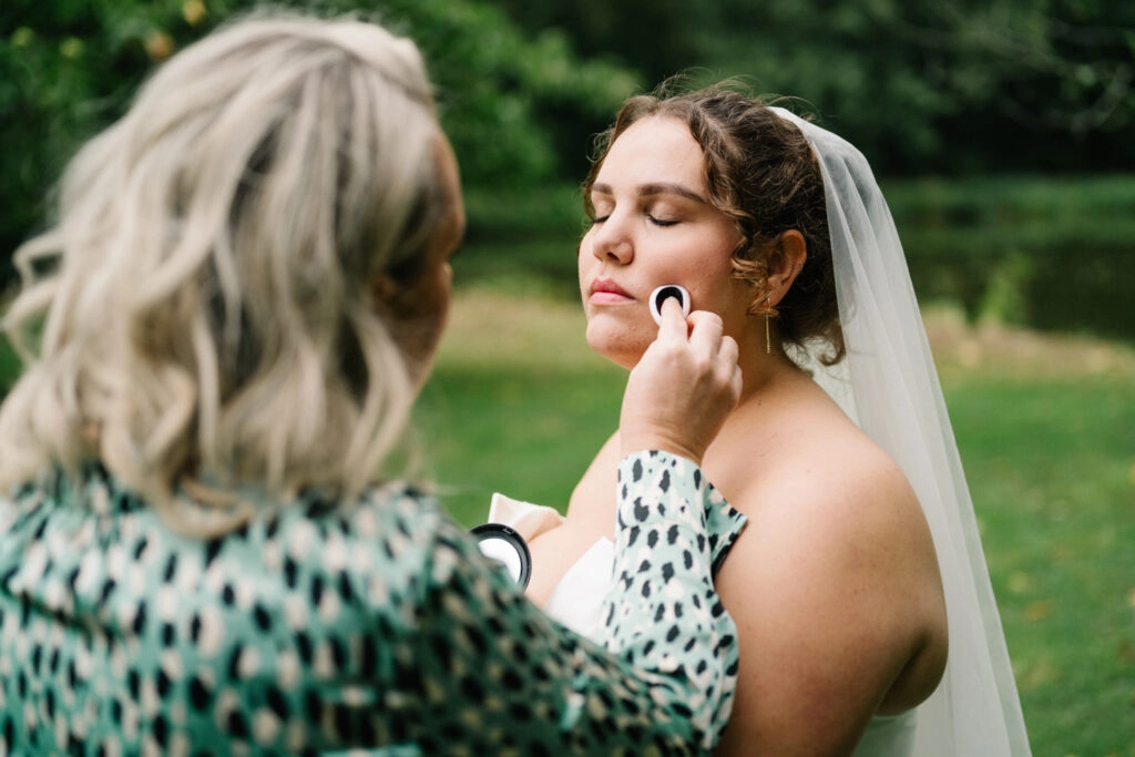 Eine Helferin frischt das Make-up der Braut auf.