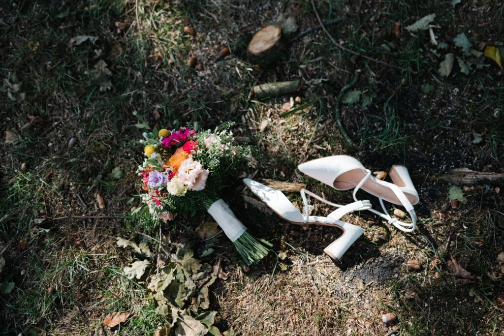 Brautschuhe und bunter Blumenstrauß liegen unter einem Baum.