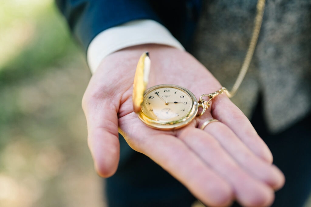 Bräutigam zeigt eine geöffnete goldfarbene Taschenuhr.