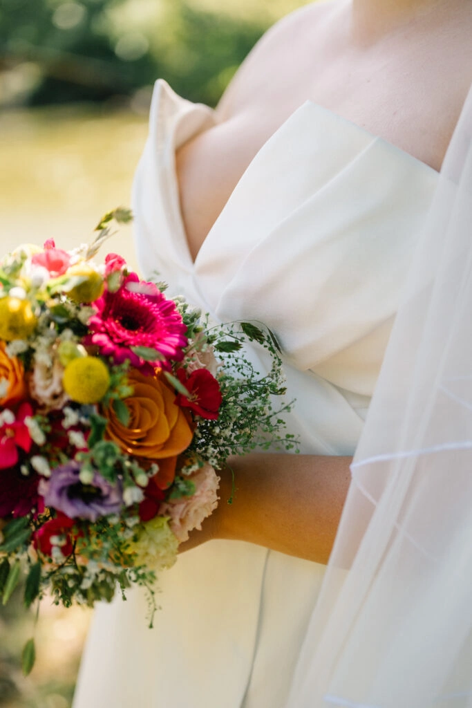 Detail von Brautkleid, Schleier und buntem Blumenstrauß.