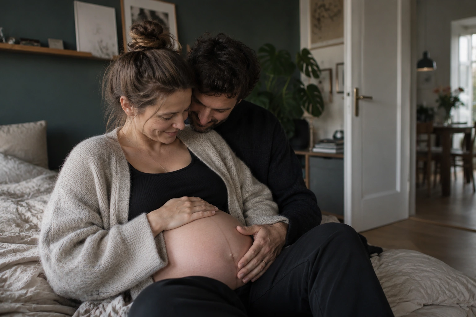 Ein Paar sitzt eng zusammen auf dem Sofa und legt die Hände auf den Babybauch.