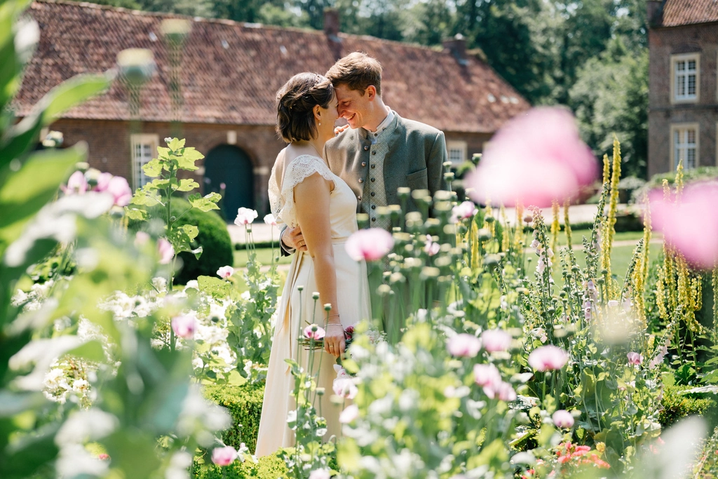 Hochzeitspaar zwischen blühenden Blumen im Garten der Wasserburg Haus Welbergen in Ochtrup.