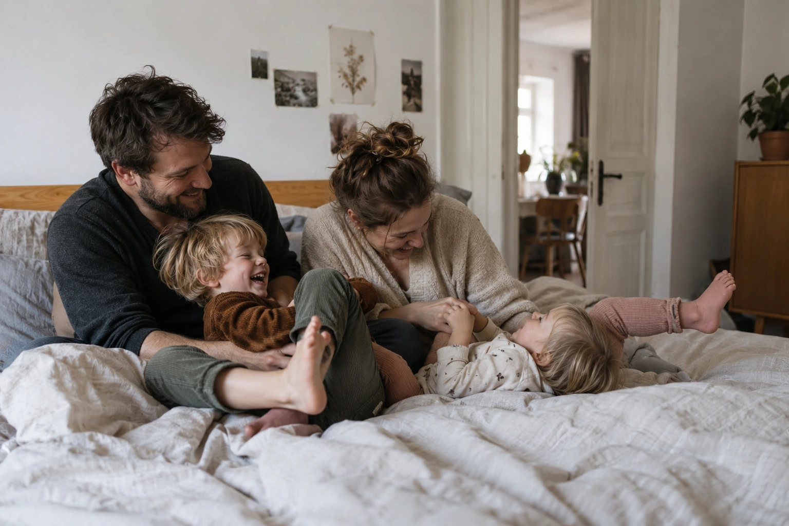 Eltern lachen mit ihren zwei Kindern auf dem Bett; ein Kind liegt auf dem Rücken.