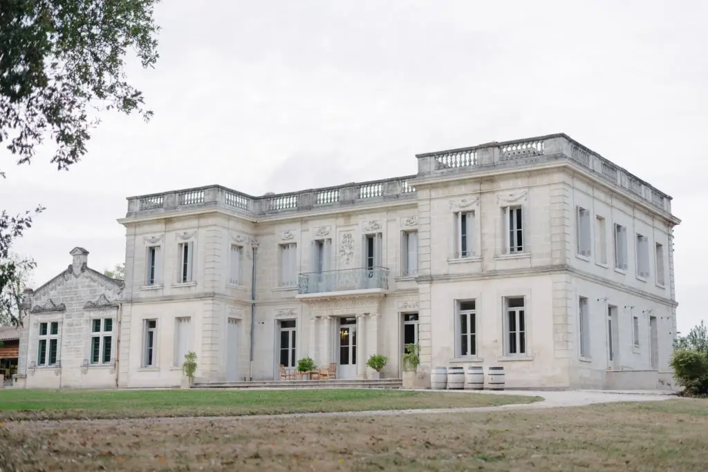 Eine historische helle Villa mit hohen Fenstern und einer Rasenfläche davor.