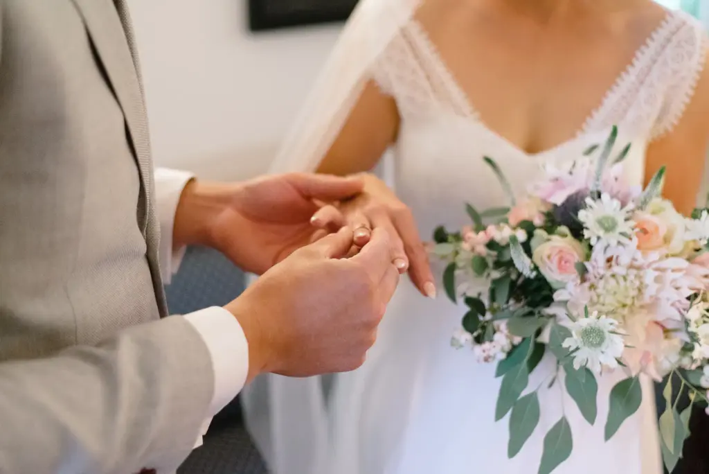 Nahaufnahme des Ringwechsels: Der Bräutigam hält die Hand der Braut neben ihrem Blumenstrauß.
