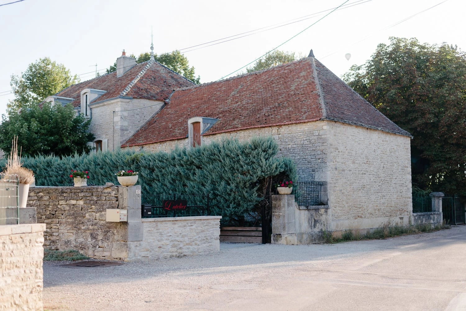 Steinhaus mit roten Ziegeldächern, bewachsener Einfahrt und Gartenmauer in der Provence.
